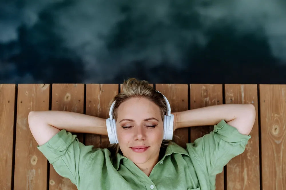 Junge Frau entspannt mit Kopfhörern auf Holzsteg, symbolisiert das Hören aller Podcastfolgen.
