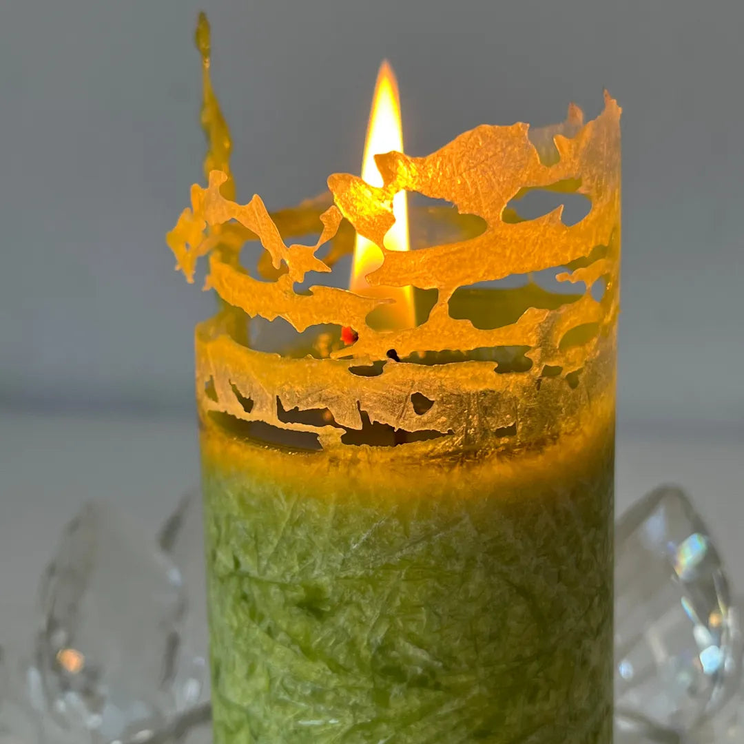 Nahaufnahme einer brennenden grünen Kerze mit leuchtendem, filigranem Abbrand-Rand.