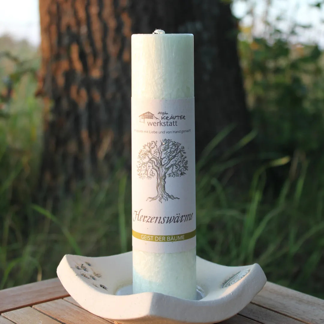 Hellgrüne Kräuterkerze "Herzenswärme" auf Kerzenteller im Freien, fördert Geborgenheit & liebende Fülle.