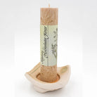 Hellbraune Allgäuer Heilkräuterkerze auf handgetöpfertem Kerzenteller mit orange-roter Mitte und Spiralverzierung.