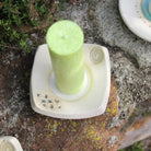 Handgetöpferter Kerzenteller mit lindgrüner Kerze, verziert mit blauen Blüten und Spirale.