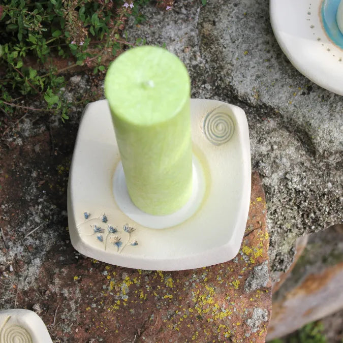 Handgetöpferter Kerzenteller mit lindgrüner Kerze, verziert mit blauen Blüten und Spirale.