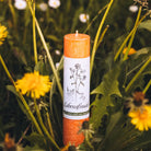 Orange Allgäuer Heilkräuterkerze "Lebensfreude" inmitten von Löwenzahn, für Frische und positive Energie.