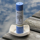 Blaue Kräuterkerze "Vision" auf Holzsteg am Wasser, schenkt Stabilität & Klarheit für persönliches Wachstum.