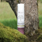 Weiß-violette Kräuterkerze "Wandlung" auf moosigem Baumstamm, stärkt Mut für bewusste Lebensveränderung.