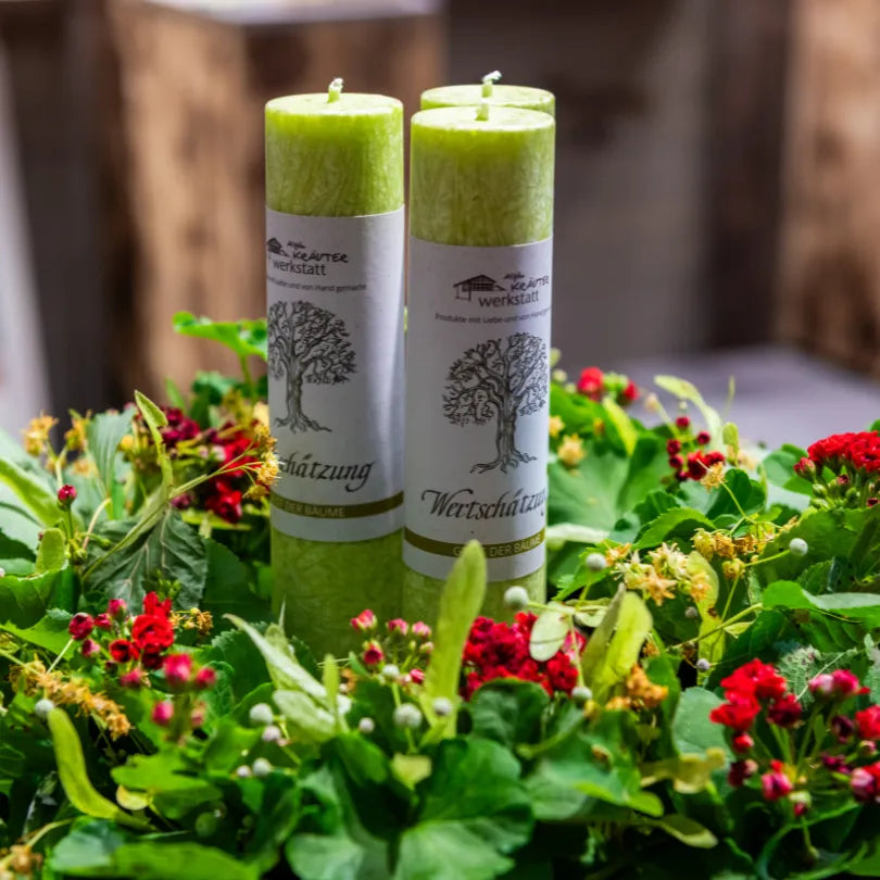 Zwei hellgrüne Kräuterkerzen "Wertschätzung" in einem Blütenkranz, symbolisieren Gemeinschaft & Verbundenheit.