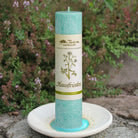 Türkise Allgäuer Heilkräuterkerze "Hausfrieden" auf Kerzenteller im Garten, für wohltuende Atmosphäre.