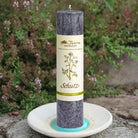 Dunkelgraue Kräuterkerze "Schutz" auf Kerzenteller, hüllt liebevoll ein & schenkt Geborgenheit in herausfordernden Phasen.