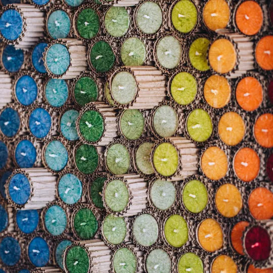 Stapel bunter Allgäuer Heilkräuterkerzen in Wellpappe-Verpackung, zeigt vielfältige Farben und Texturen.