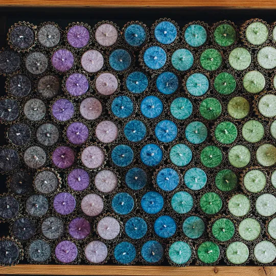 Draufsicht auf eine Anordnung von vielen kleinen bunten Kerzen in Kartonverpackung, symbolisiert Vielfalt & Handwerkskunst.