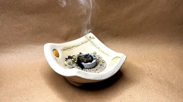 Räuchern mit Kohle: Glimmende Räucherkohle auf Räuchersand im Keramikteller mit aufsteigendem Rauch.