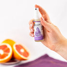 Hand hält Baldini Buddhaduft Aura & Bodyspray, harmonisierend und entspannend, mit Grapefruits.