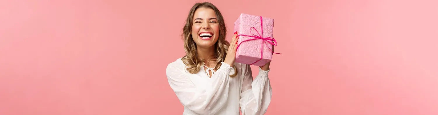 Lachende Frau hält pinkes Geschenkpaket, symbolisiert Freude, Neuigkeiten und Rabatte vom Sera Benia Verlag.