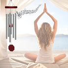 Windspiel mit Notenlinien, symbolisiert Ruhe und Entspannung bei meditierender Frau am Strand.