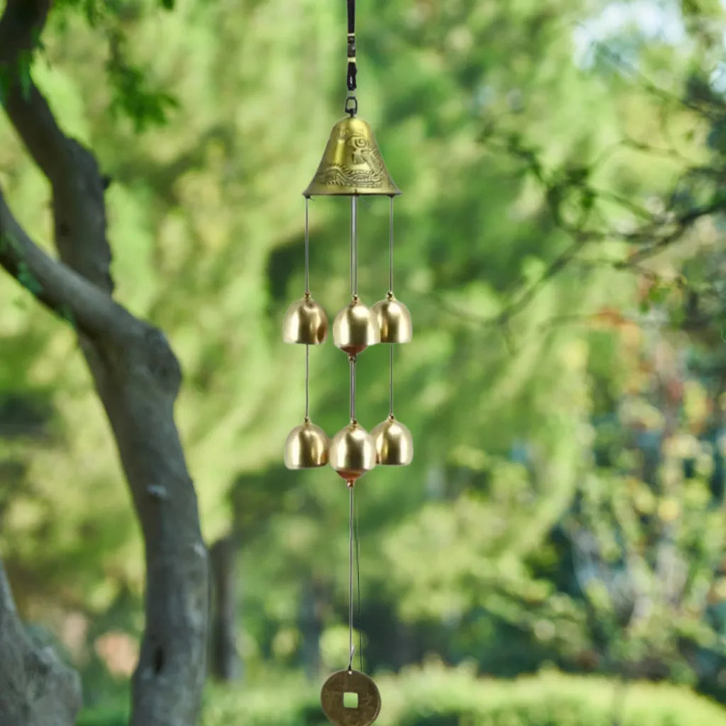 Goldfarbenes Glocken-Windspiel mit 8 kleinen Glocken vor grünem Baumbestand.