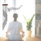 Windspiel mit spiralförmigen Röhren und Notenlinien, symbolisiert Frieden und Harmonie bei meditierender Frau.