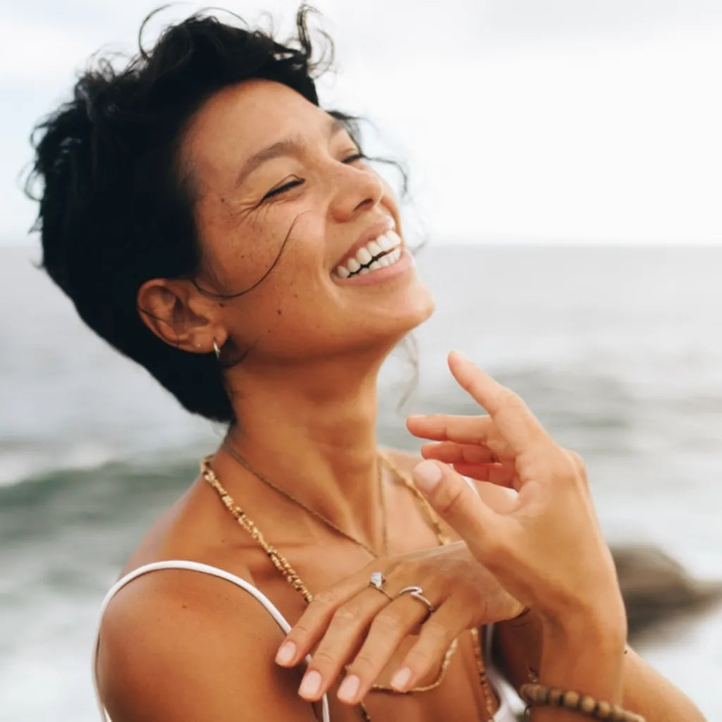 Frau lacht entspannt am Meer, symbolisiert Wohlbefinden & Balance durch Autogenes Training & Tiefenentspannung.
