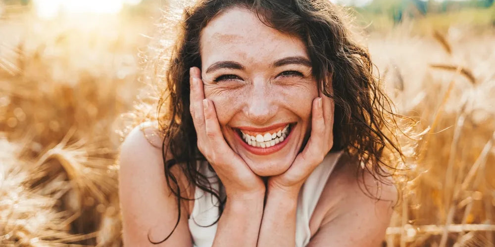 Eine glückliche, lachende Frau mit Händen am Gesicht in einem sonnigen Weizenfeld, symbolisierend Dankbarkeit, Fülle und Lebensfreude, passend zum Thema Gebet und positive Einstellung.