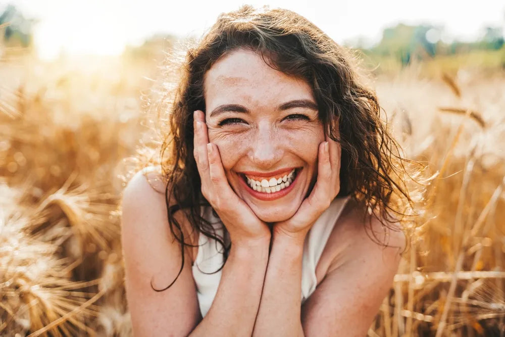 Eine glückliche, lachende Frau mit Händen am Gesicht in einem sonnigen Weizenfeld, symbolisierend Dankbarkeit, Fülle und Lebensfreude, passend zum Thema Gebet und positive Einstellung.