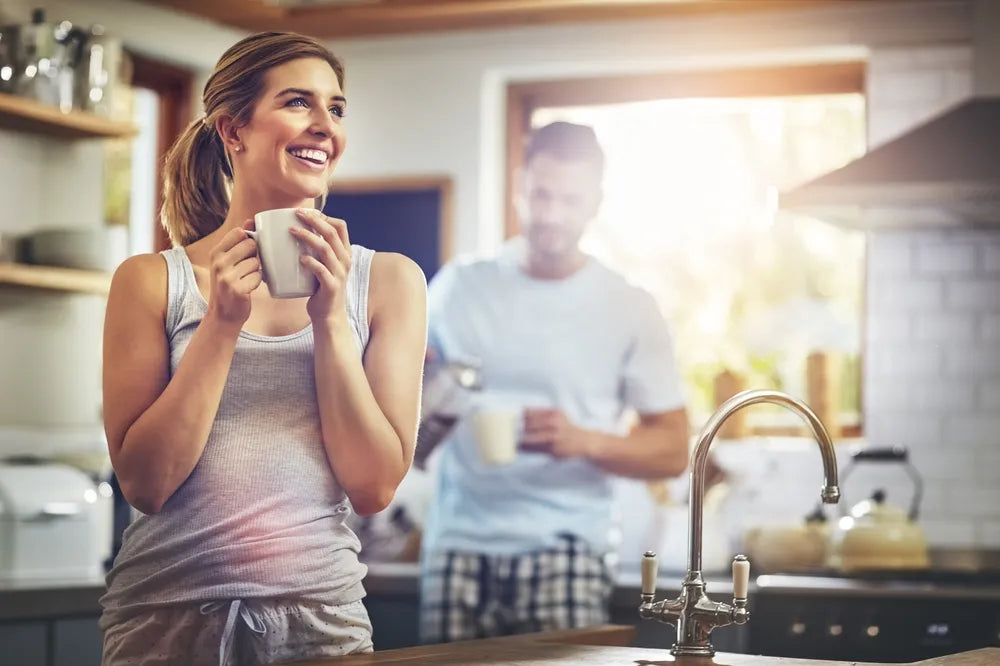 Frau steht mit ihrem Morgen-Kaffee in der Küche und freut sich