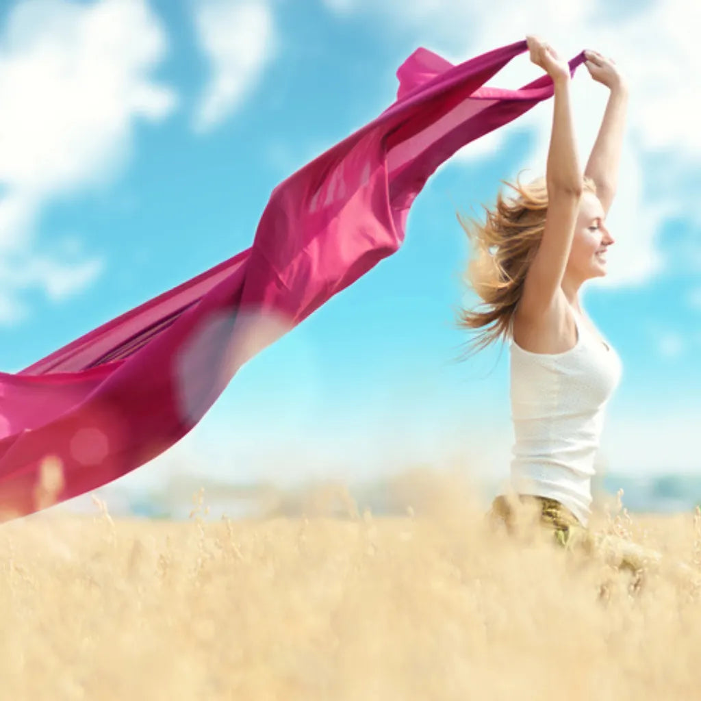 Frau mit wehendem Tuch im Feld, symbolisiert Lebensfreude, Freiheit und neue Energie.