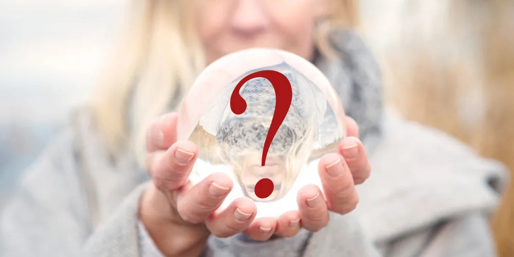 Eine Frau hält eine Glaskugel in den Händen, in der ein rotes Fragezeichen reflektiert wird, symbolisiert die Suche nach dem Sinn des Lebens.