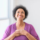 Frau mit Händen auf Brust blickt hoffnungsvoll, symbolisiert Heilung, Frieden und Erneuerung.