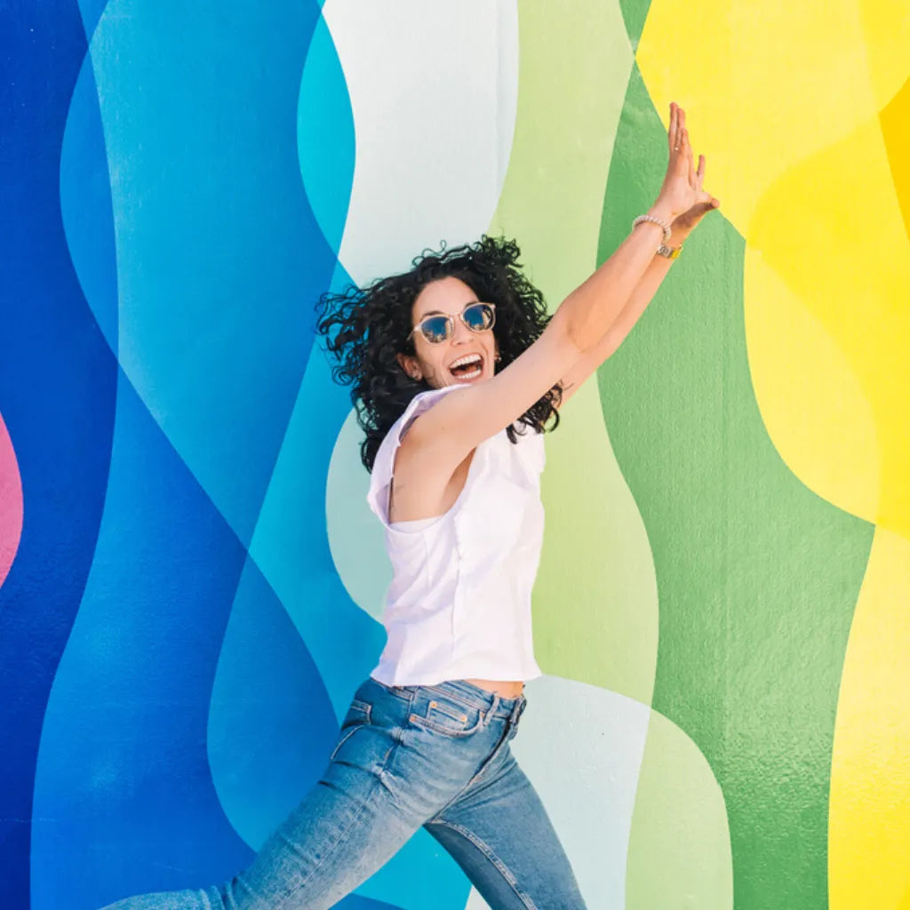 Frau voller Lebensfreude springt vor bunter Wand. Energie, mentale Stärke.