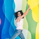 Frau voller Lebensfreude springt vor bunter Wand. Energie, mentale Stärke.