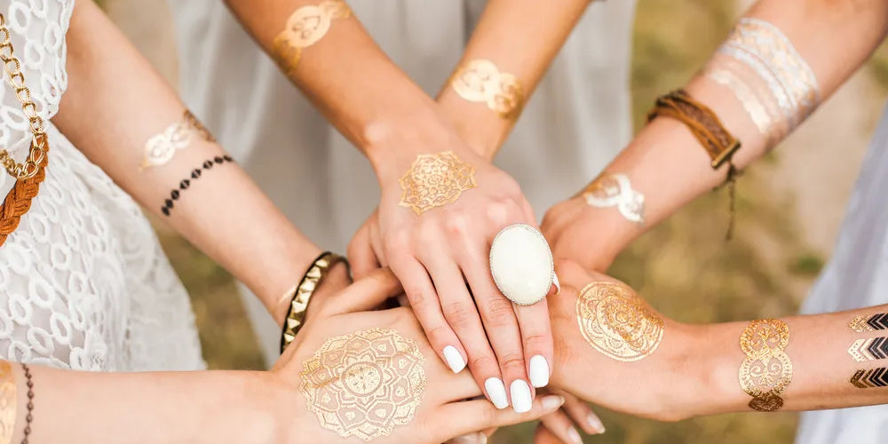 Frauenhände, die zum Schwur aufeinander liegen mit goldenen Tattoos, symbolisieren Einheit und Verbundenheit.