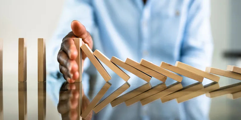 Eine Hand stoppt eine Reihe fallender Dominosteine, symbolisierend das Setzen von Grenzen, Krisenmanagement oder das Verhindern negativer Kettenreaktionen.