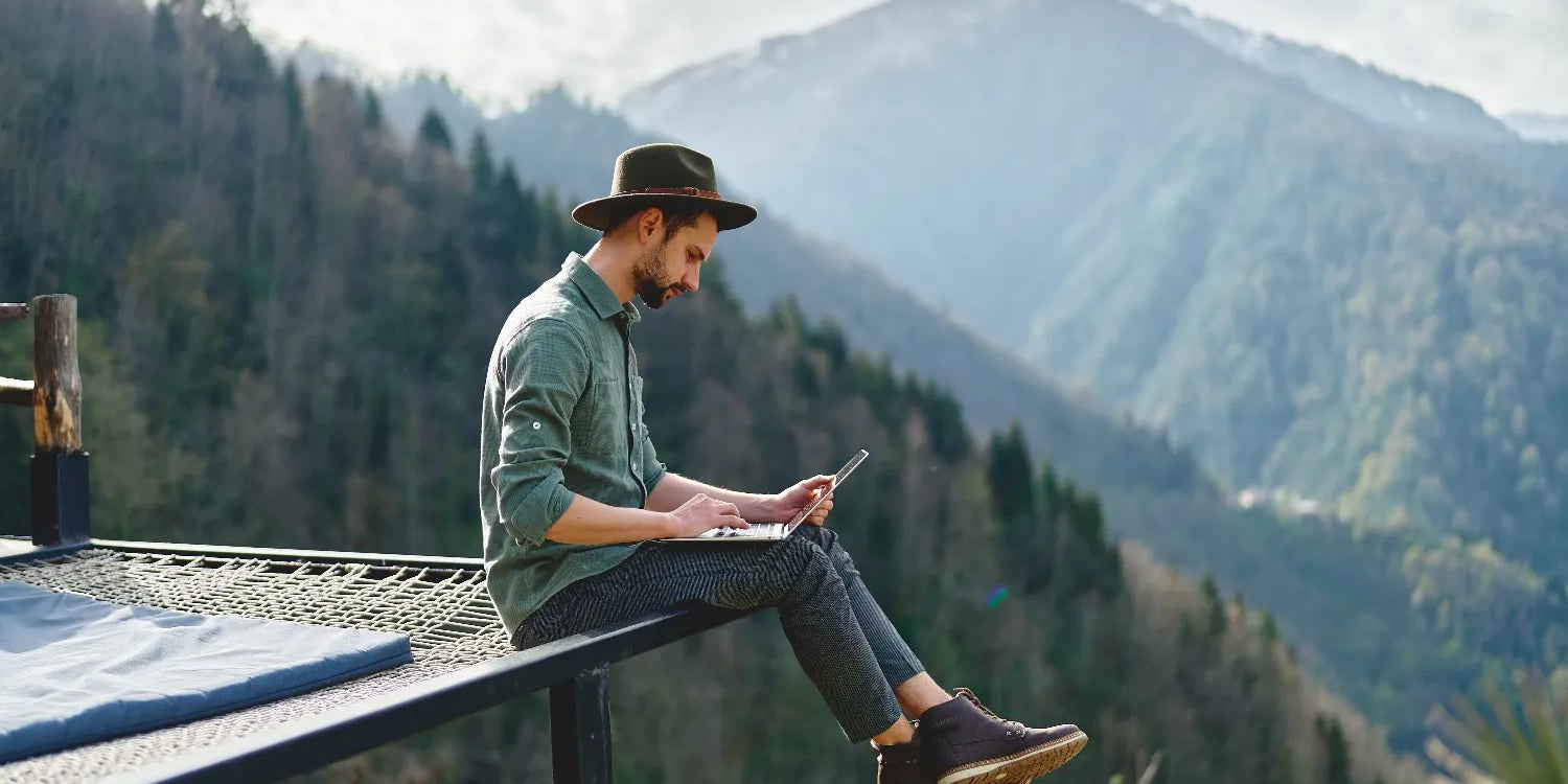 Mann sitzt in der Natur am Laptop, um ihn Bergpanorama