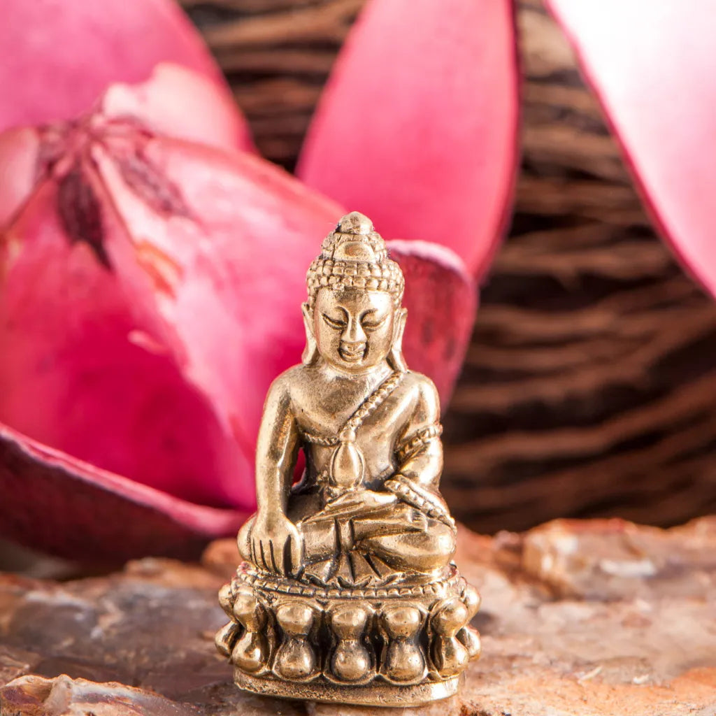 Goldfarbene Miniatur Medizinbuddha Figur auf Stein, umgeben von rosa Lotusblüten, für Meditation und Dekoration.