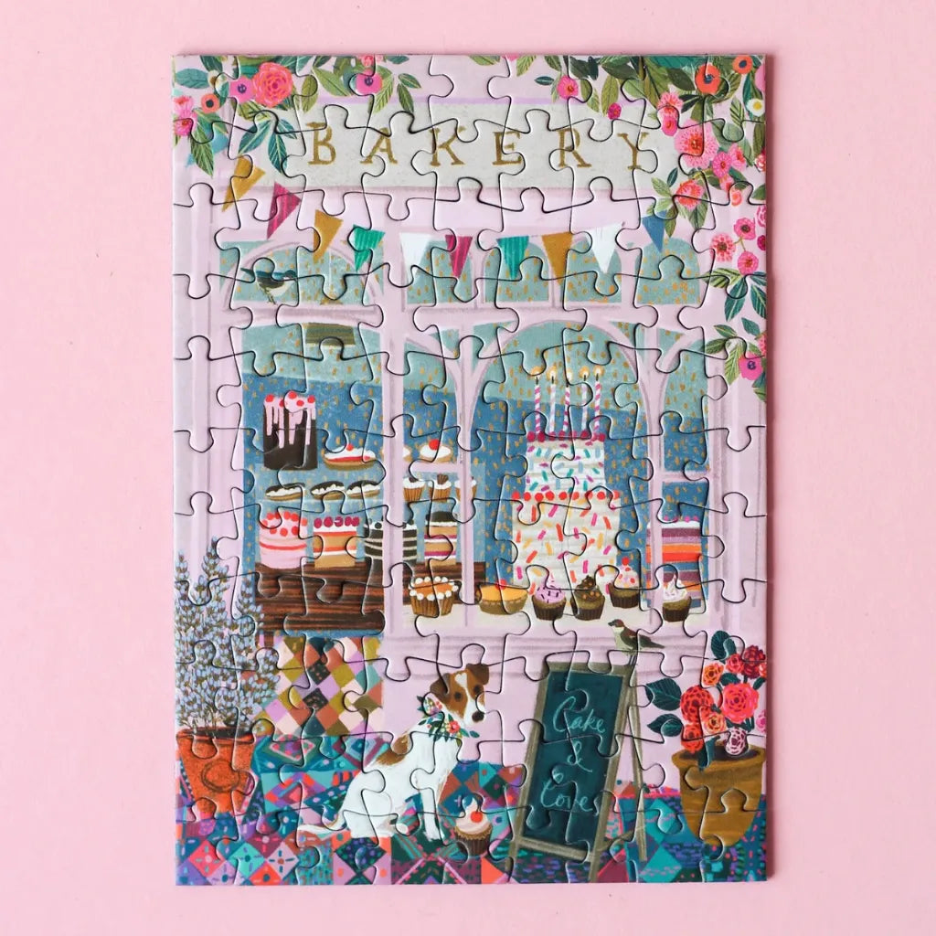 Fertig gelegtes Piecely Minipuzzle 99 Teile "Cake & Love". Das farbenfrohe Motiv zeigt eine liebevoll gestaltete Bäckerei mit vielen Leckereien, einem Hund und blühenden Pflanzen.