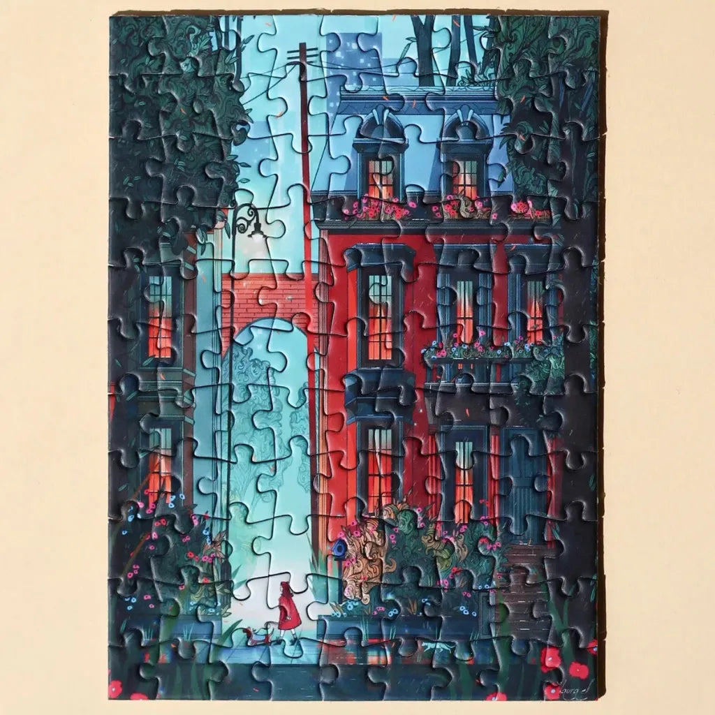 Fertig gelegtes Piecely Minipuzzle 99 Teile "Midnight Walk". Das Motiv zeigt eine nächtliche Straßenszene mit einem roten Haus, Bäumen und einer Frau im roten Mantel unter Straßenlaternen.
