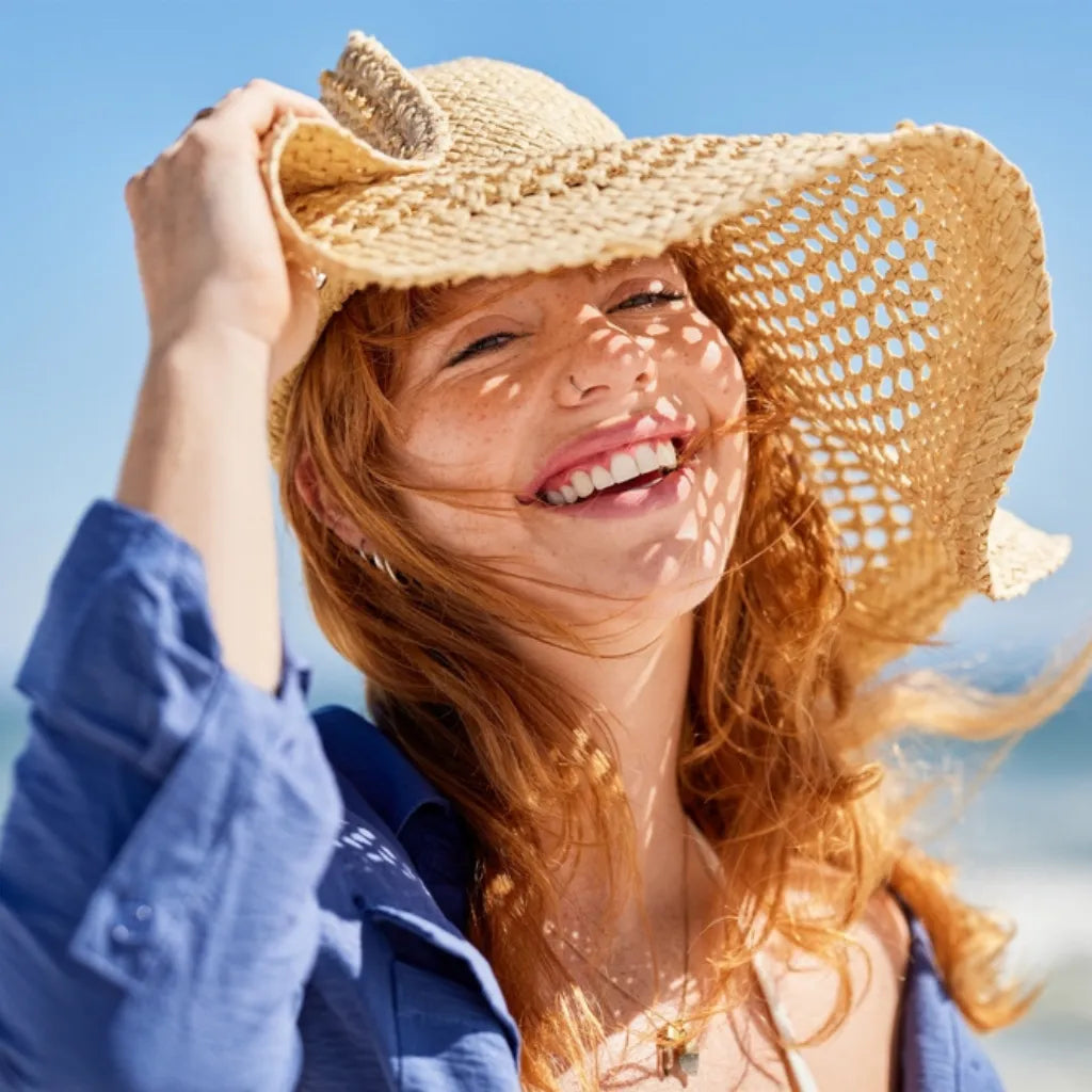 Frau lacht glücklich am Strand mit Strohhut, symbolisiert Entspannung & Urlaub durch PMR am Meer.