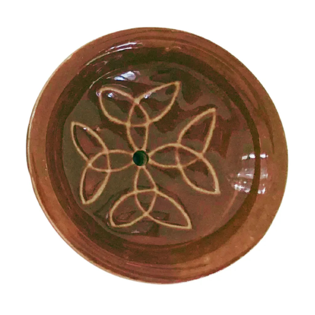 Nahaufnahme eines runden Keramik Räucherstäbchenhalters in warmem Dunkelbraun, verziert mit einem harmonischen weißen Knotenmuster und einem zentralen Loch für Räucherstäbchen.