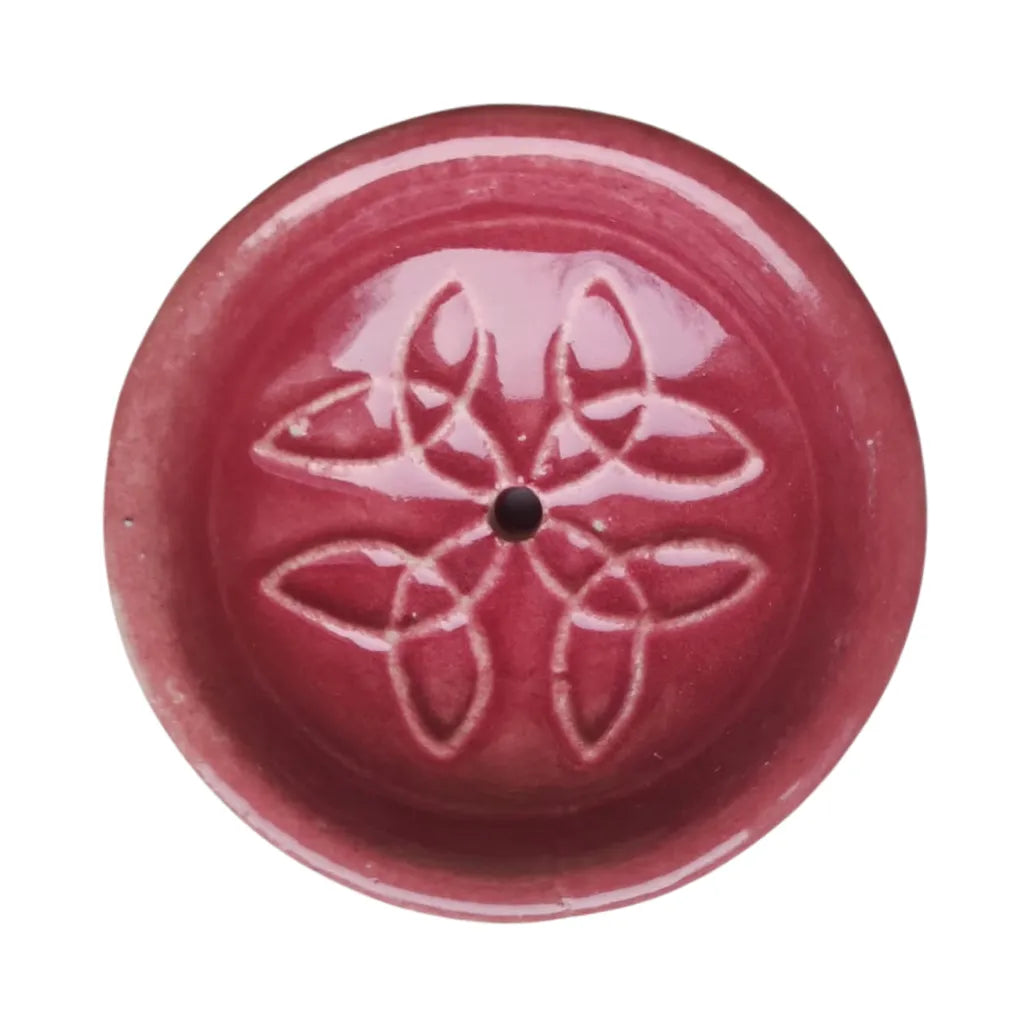 Nahaufnahme eines runden Keramik Räucherstäbchenhalters in lebhaftem Rot, verziert mit einem harmonischen weißen Knotenmuster und einem zentralen Loch für Räucherstäbchen.