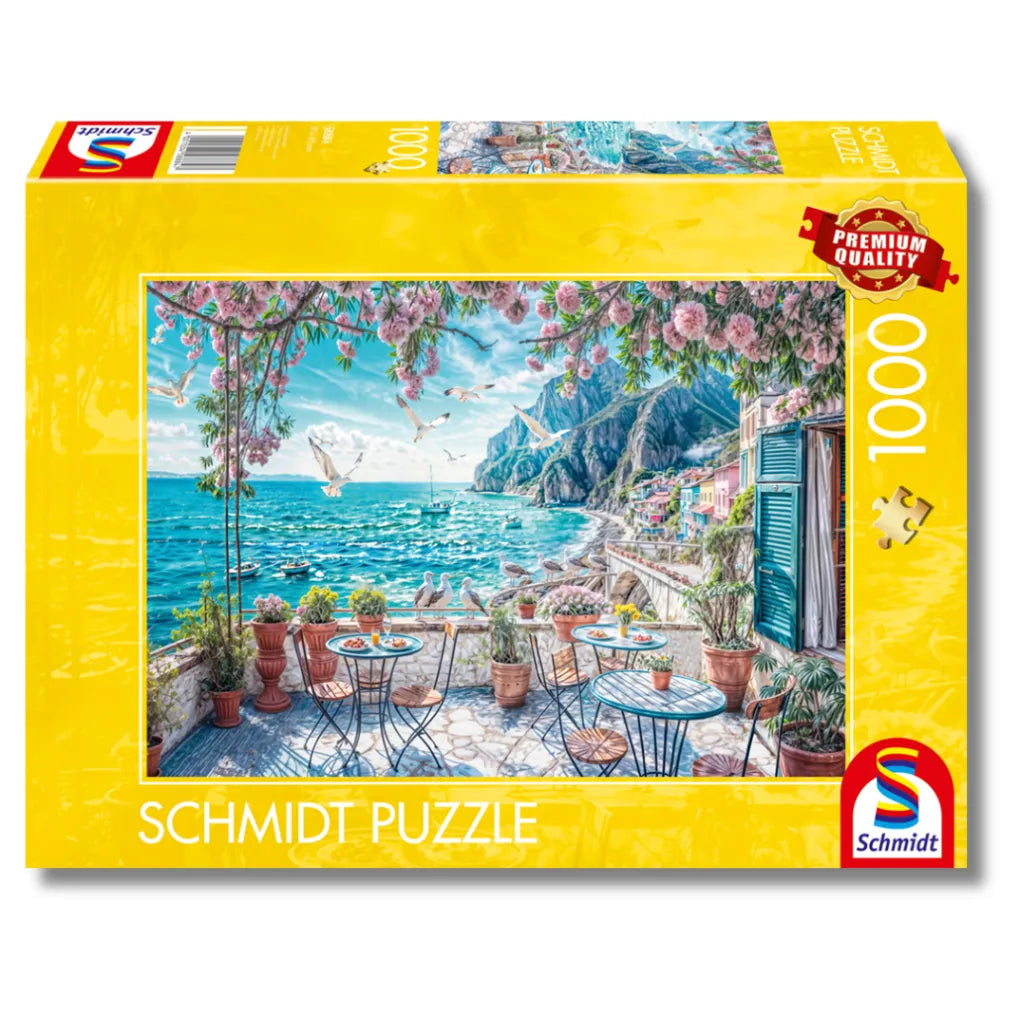 Schmidt Puzzle 1000 Teile "Terrasse am Meer" Produktverpackung. Zeigt ein idyllisches Küstenmotiv mit Balkon, Meer und blühenden Blumen.
