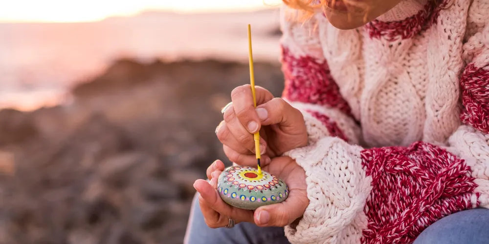 Person bemalt Stein mit Mandala-Muster, symbolisiert Kreativität und Achtsamkeit.