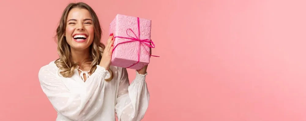 Lachende Frau hält pinkes Geschenkpaket, symbolisiert Freude, Neuigkeiten und Rabatte vom Sera Benia Verlag.