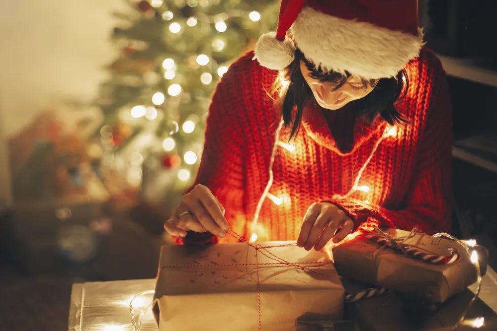 Frau mit Weihnachtsmütze packt freudig Weihnachtsgeschenke