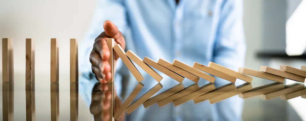 Eine Hand stoppt eine Reihe fallender Dominosteine, symbolisierend das Setzen von Grenzen, Krisenmanagement oder das Verhindern negativer Kettenreaktionen.