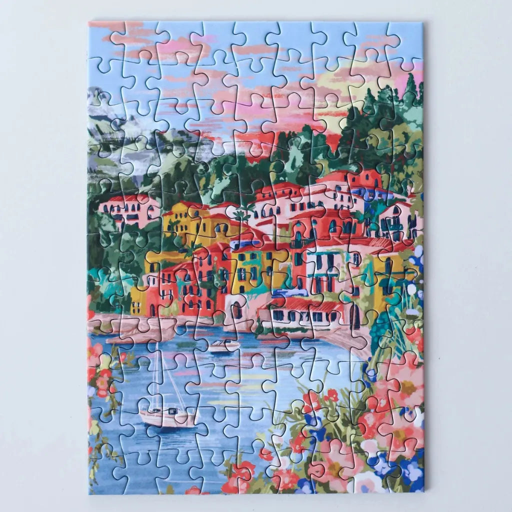 Das vollständig gelegte 99 Teile Piecely Minipuzzle "Lake Como". Eine leuchtende Darstellung des malerischen italienischen Sees mit farbenfrohen Gebäuden, Bergen und einem Segelboot im Wasser.