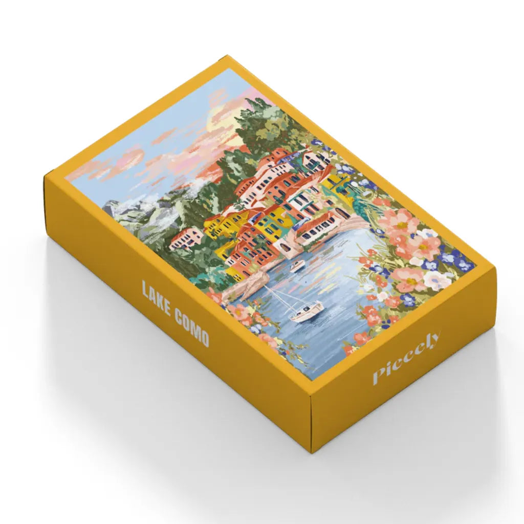 Schrägansicht der gelben Verpackung des 99 Teile Piecely Minipuzzles "Lake Como". Die Box zeigt die charmante Illustration des Comer Sees