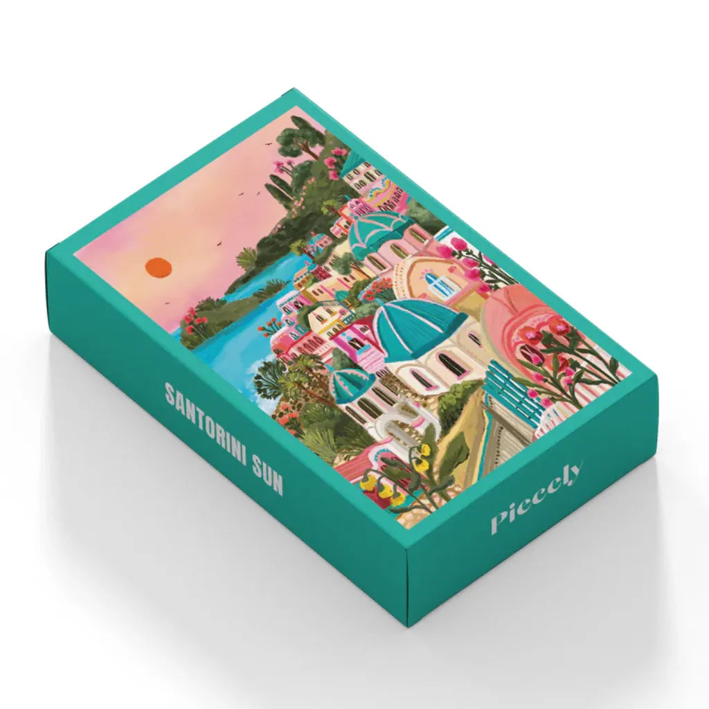 Schrägansicht der Verpackung des 99 Teile Piecely Minipuzzles "Santorini Sun". Die türkisfarbene Box zeigt das Motiv der bunten Inselhäuser und den Titel des Puzzles auf der Seite.