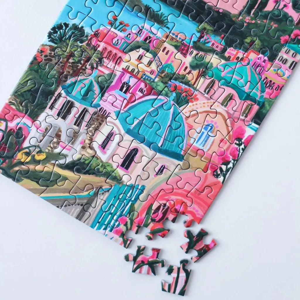 Teilweise gelegtes Piecely Minipuzzle 99 Teile "Santorini Sun". Zeigt bunte Häuser, türkise Kuppeln und das Mittelmeer. Lose Puzzleteile im Vordergrund des charmanten Santorini-Motivs.