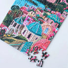 Teilweise gelegtes Piecely Minipuzzle 99 Teile "Santorini Sun". Zeigt bunte Häuser, türkise Kuppeln und das Mittelmeer. Lose Puzzleteile im Vordergrund des charmanten Santorini-Motivs.