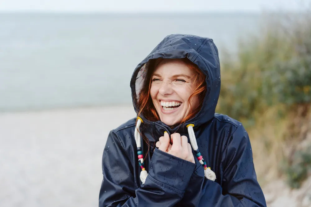 Lachende Frau am Strand symbolisiert Motivation und Lebensfreude, um Ziele zu erreichen.